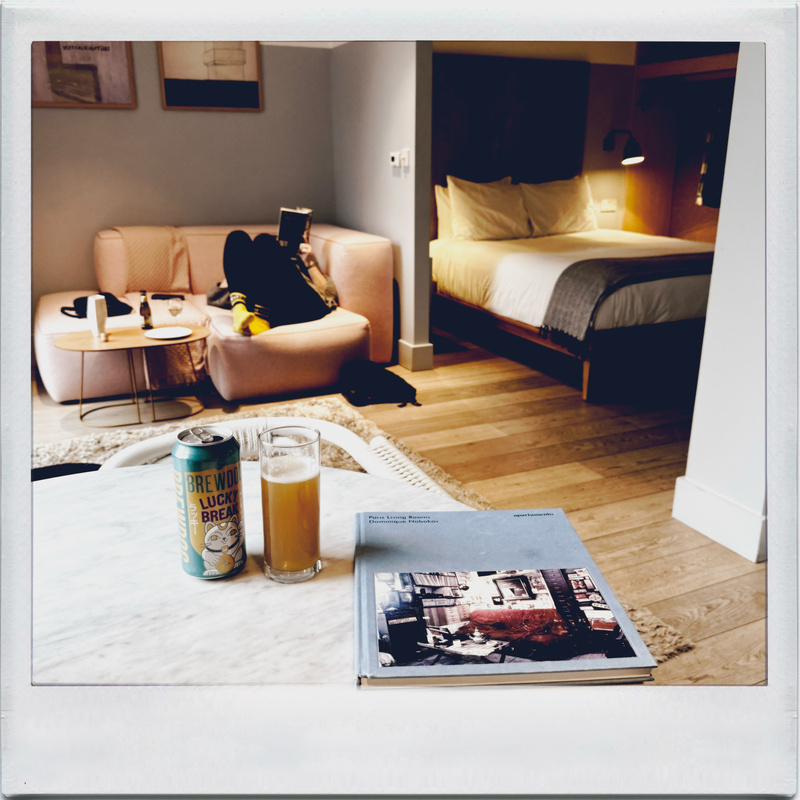 Auto-generated description: A cozy living space is depicted with a person relaxing on a couch, a can and glass of beer on the table, and a book beside them.