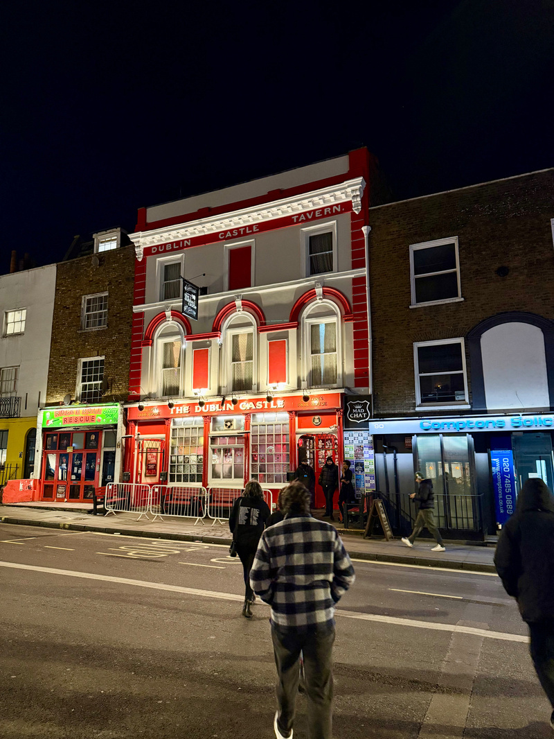 Auto-generated description: A group of people walk in front of the brightly lit Dublin Castle Tavern and surrounding buildings on a dimly lit street at night.