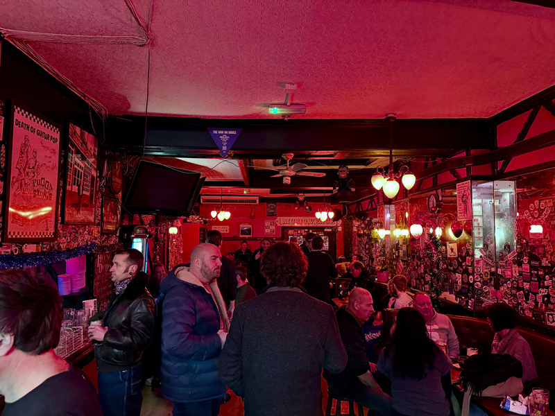 Auto-generated description: A group of people socializes inside a dimly lit bar with red lighting, decorated with various posters and memorabilia.