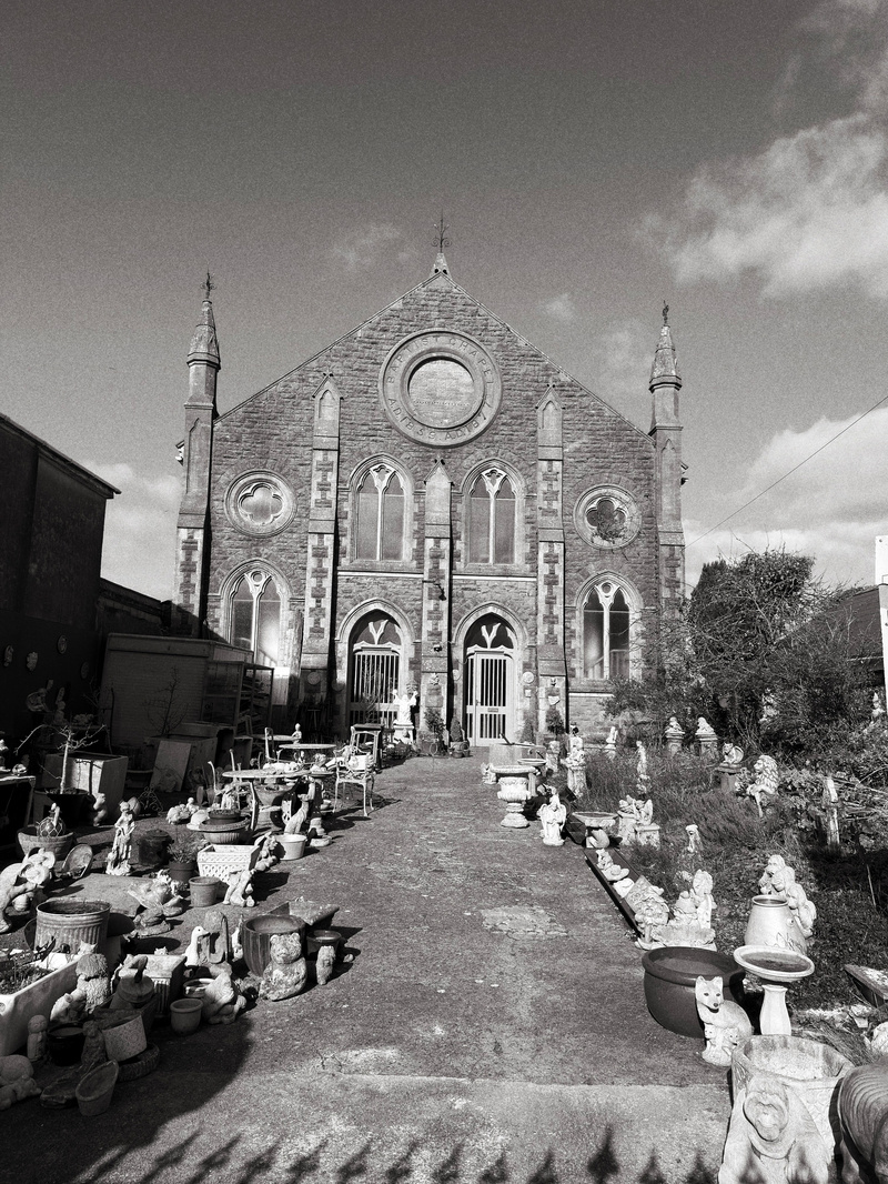 Auto-generated description: A historic building with arched windows and twin spires stands as the backdrop to a pathway lined with various statues and garden ornaments.
