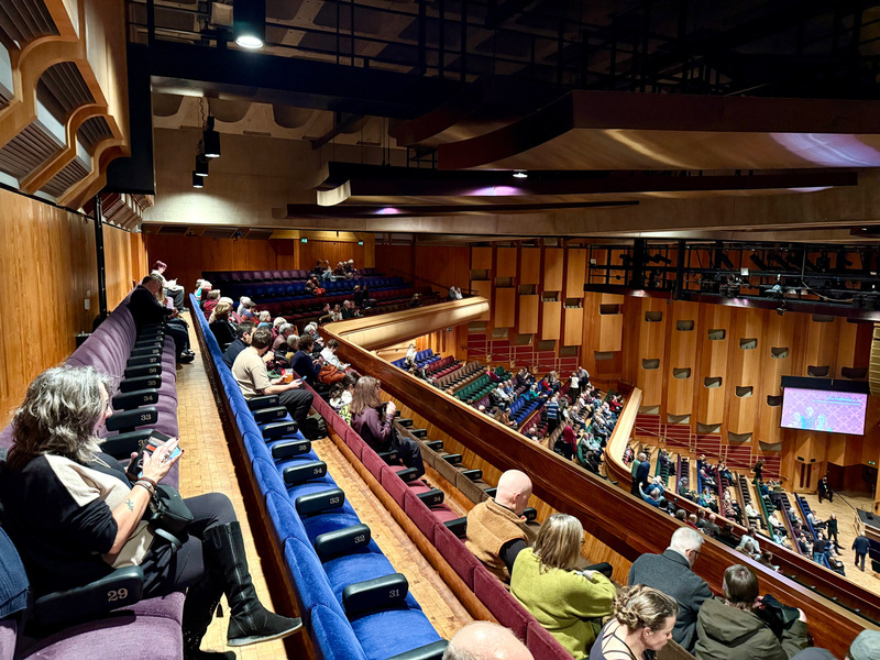 Auto-generated description: People are seated in the upper balcony of a concert hall, waiting for a performance to begin.