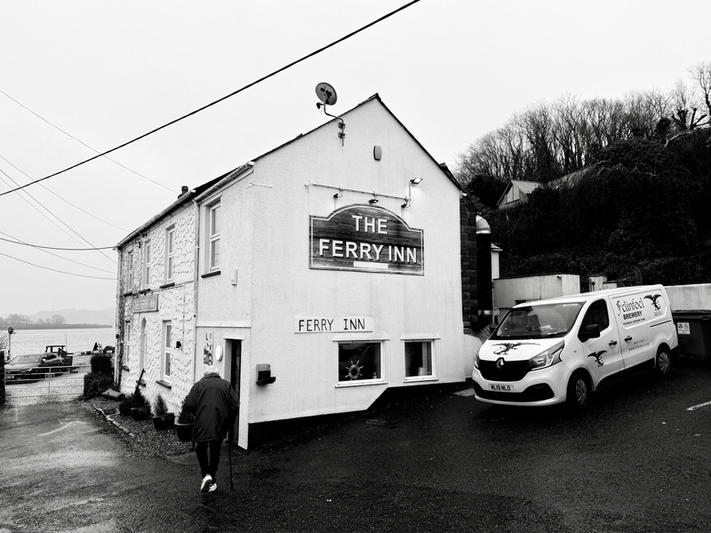Auto-generated description: A person walking by a waterfront building labeled The Ferry Inn, with a parked van nearby on an overcast day.