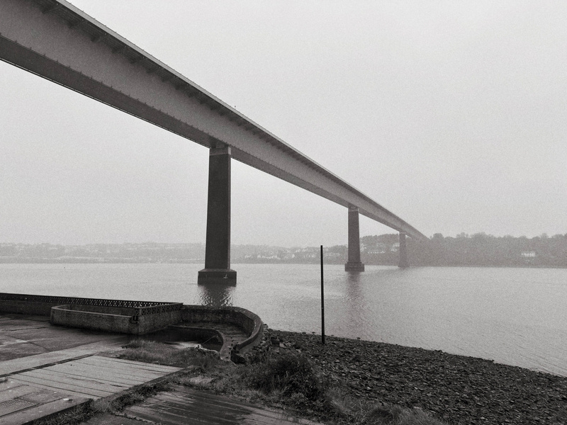 Auto-generated description: A long bridge stretches across a foggy body of water, supported by tall pillars, with a shoreline in the foreground.
