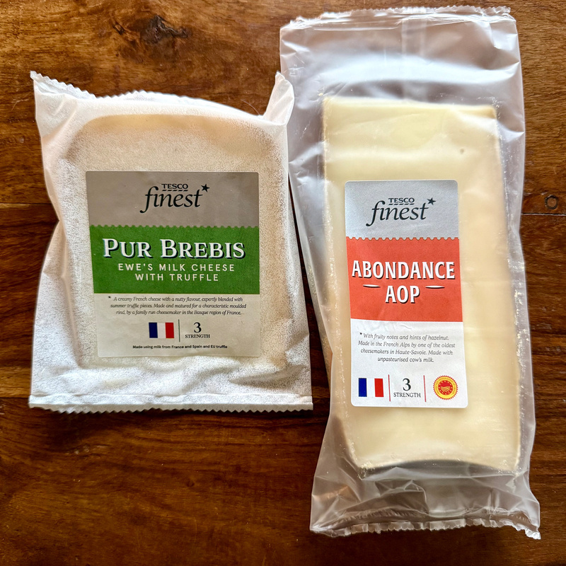 Two packages of Tesco Finest French cheese are displayed on a wooden surface, one labeled Pur Brebis (ewe's milk cheese with truffle) and the other Abondance AOP.