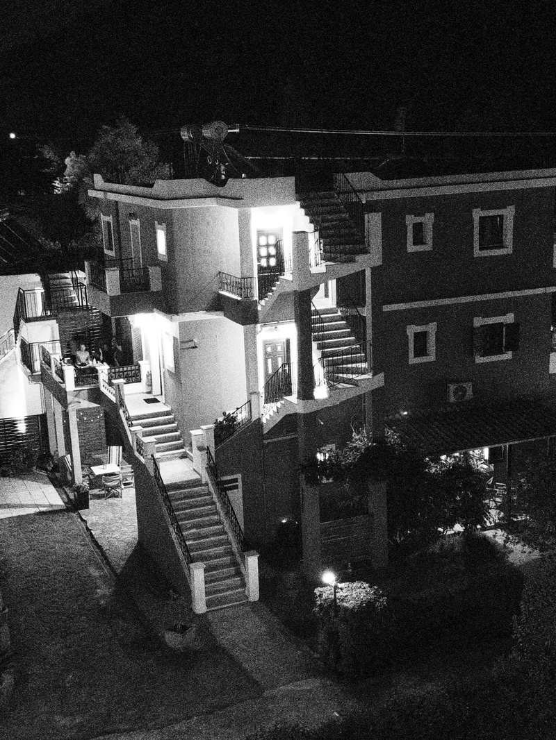 Auto-generated description: A multi-story building with external staircases and illuminated windows is captured at night in black and white.